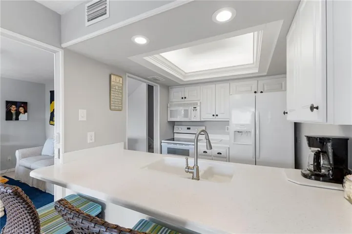 Kitchen with a raised ceiling, white cabinetry, white appliances, a kitchen breakfast bar, and recessed lighting