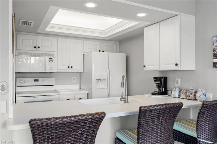 Kitchen featuring a tray ceiling, white appliances, white cabinets, a peninsula, and crown molding