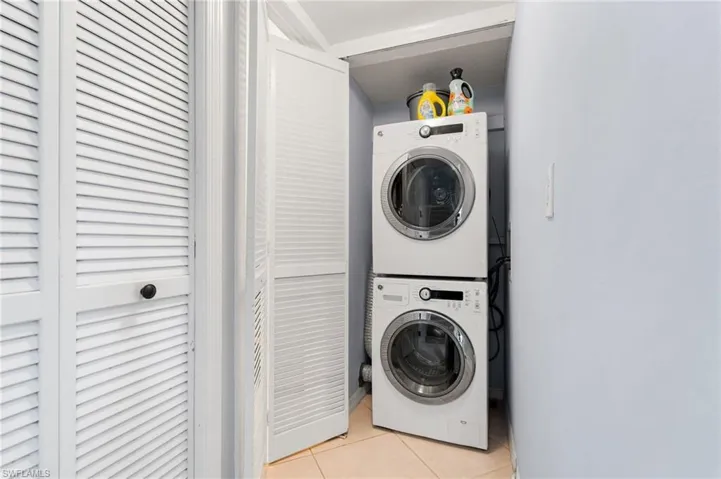 Laundry area with light tile patterned floors and stacked washing machine and dryer