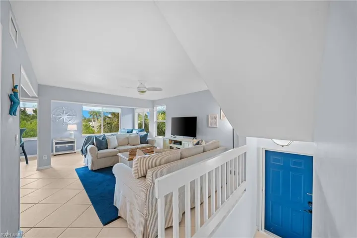 Vaulted ceiling, ceiling fan, tile flooring, white banister, and blue door