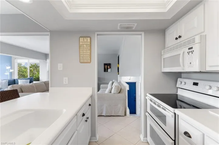 Kitchen with white appliances, white cabinetry, light tile patterned floors, and ornamental molding