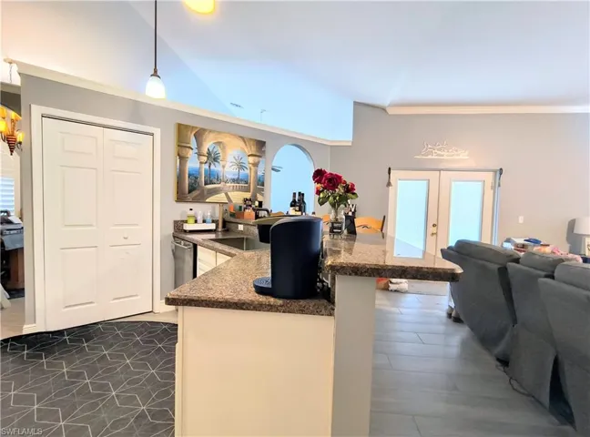Kitchen with french doors, crown molding, stone counters, hanging light fixtures, and lofted ceiling