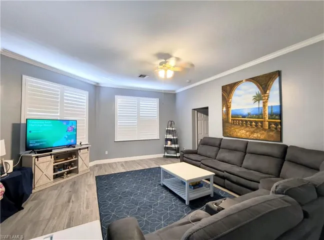 Living room with ceiling fan, light wood-type flooring, and crown molding