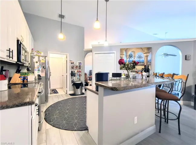 Kitchen featuring white cabinetry, a kitchen breakfast bar, light wood tile flooring, range with electric cooktop, and pendant lighting