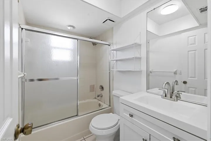 Full bathroom featuring a tub-shower combination with sliding frosted glass doors, white tile surround, a single vanity with an integrated sink, brushed nickel fixtures, and a large wall-mounted mirror