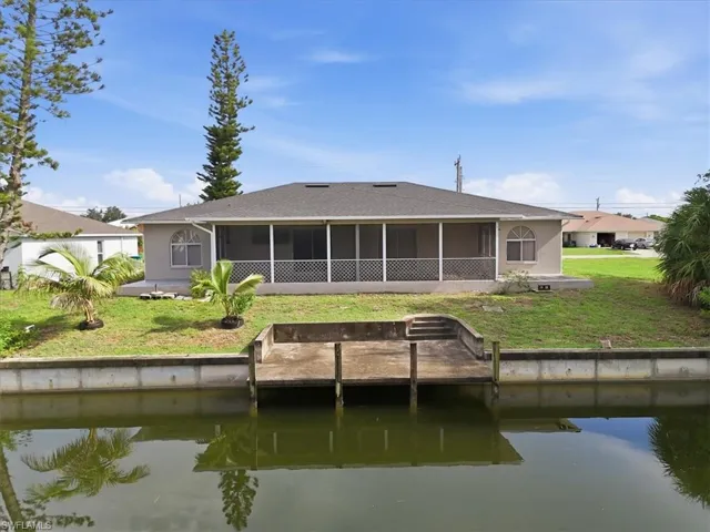 Waterfront residence featuring a screened-in patio, backyard with mature trees, and a concrete dock