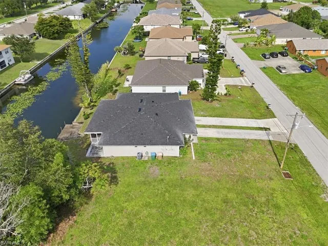 Waterfront property featuring a private boat dock, screened lanai, concrete driveway, and established landscaping