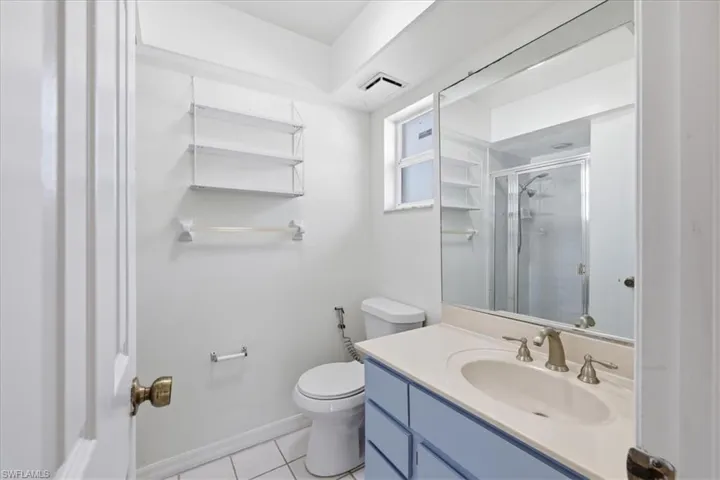 Bathroom featuring a built-in vanity with a light-colored countertop and undermount sink, a large mirror, a shower with a glass enclosure, a window, and white tile flooring