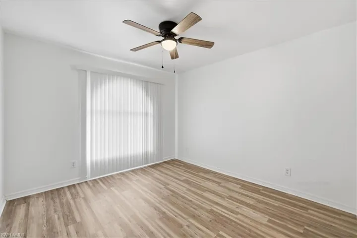 Neutral white walls with crown molding, wood-finish flooring, a ceiling fan with integrated lighting, and vertical blinds covering a large window