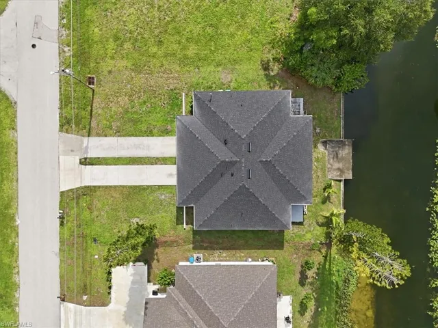 Property featuring a shingle roof, concrete driveway, and canal frontage with a dock structure
