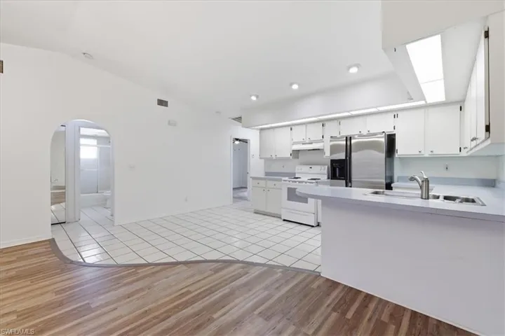 Open-concept kitchen featuring white cabinetry, stainless steel refrigerator, and white appliances