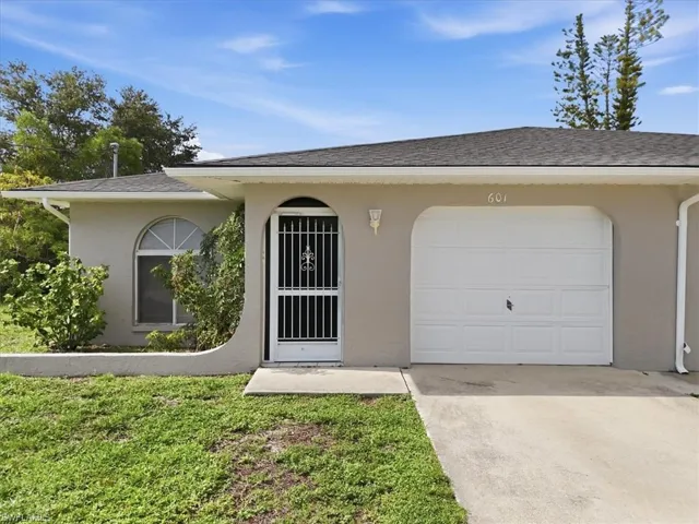 Single-story stucco exterior featuring a white garage door, arched entryway with a security screen door, and an arched window