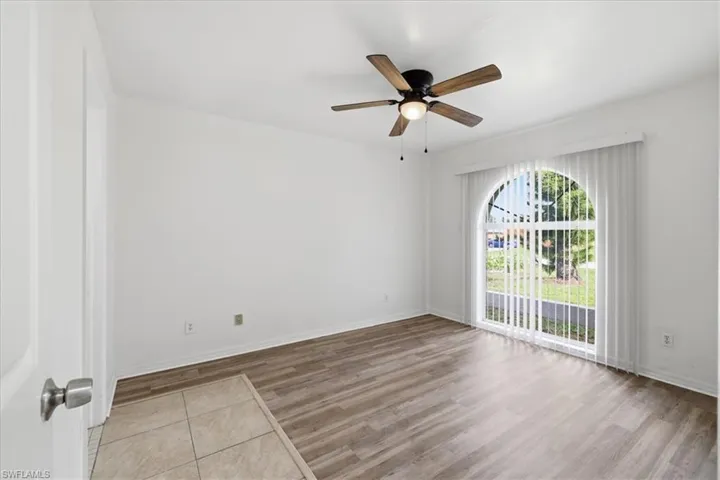 Room featuring wood-finish flooring, a contemporary ceiling fan with integrated lighting, and an arched window with vertical blinds