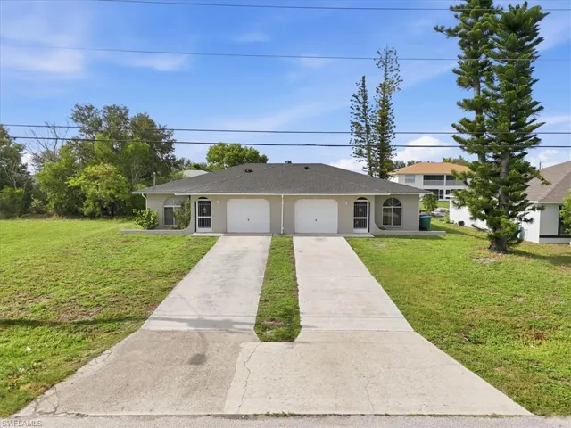 Duplex property featuring a neutral stucco exterior, dark shingle roof, arched window details, two separate driveways, and individual garage entrances