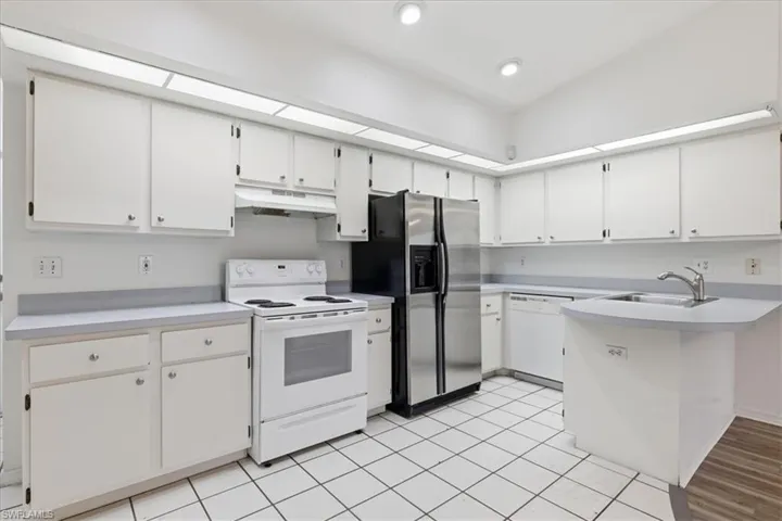 Kitchen featuring white cabinetry, light countertops, white tile flooring, stainless steel refrigerator, and white range