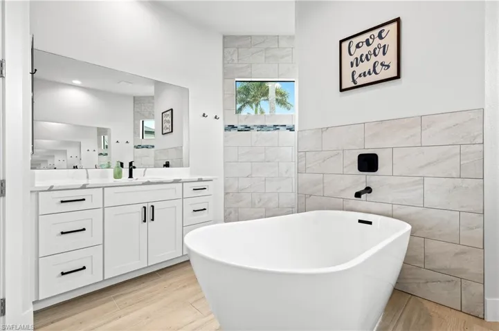 Bathroom featuring vanity, a freestanding bath, light wood finished floors, tile walls, and walk in shower