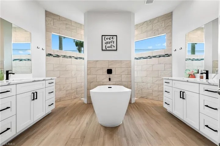 Full bathroom featuring tile walls, two vanities, a walk in shower, a soaking tub, and light wood-type flooring
