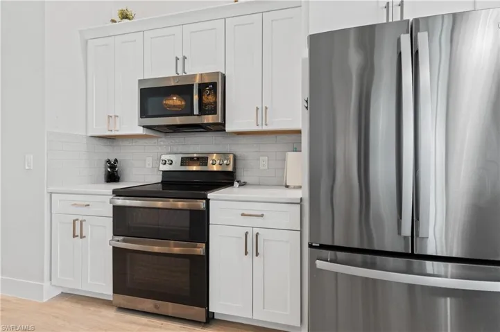 Kitchen with stainless steel appliances, white cabinetry, and decorative backsplash
