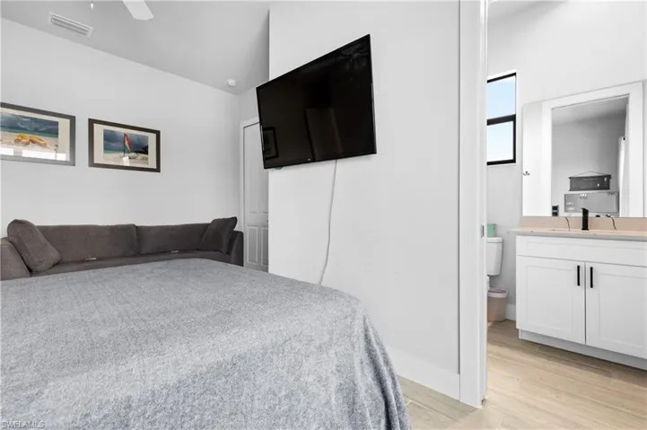 Bedroom featuring light wood-type flooring, ensuite bath, ceiling fan, and vaulted ceiling