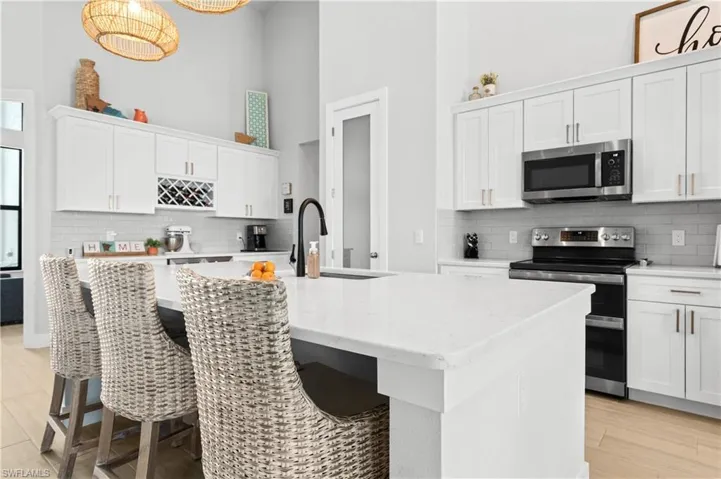 Kitchen with stainless steel appliances, a breakfast bar area, white cabinetry, light stone countertops, and a high ceiling
