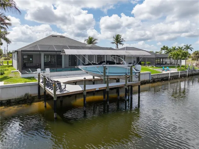 Dock area featuring glass enclosure, a water view, boat lift, a sunroom, and an outdoor pool
