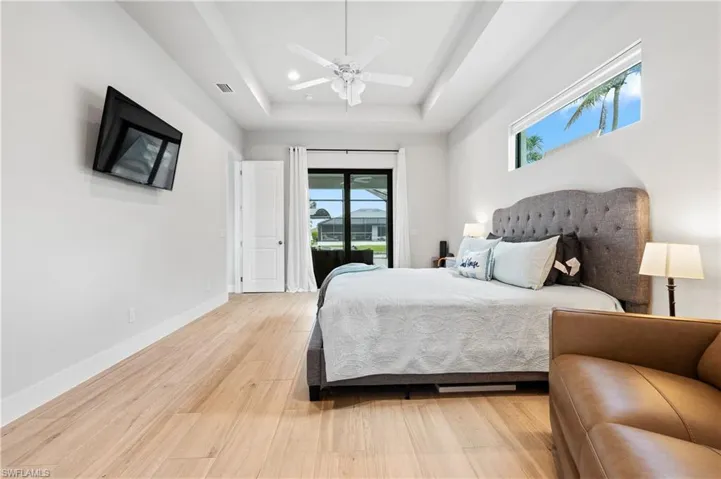 Bedroom featuring access to exterior, a tray ceiling, light wood-style floors, and ceiling fan
