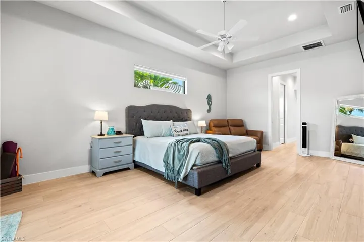 Bedroom featuring a raised ceiling, light wood-style flooring, and ceiling fan
