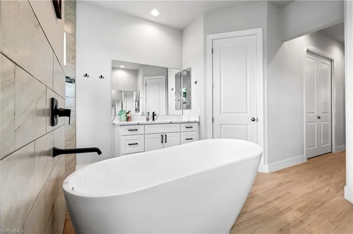 Full bathroom featuring a soaking tub, light wood-style flooring, vanity, and recessed lighting