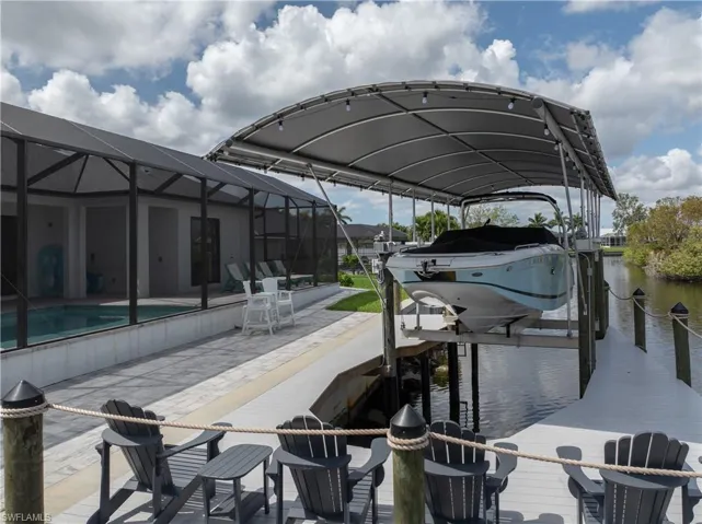 Dock area featuring boat lift, glass enclosure, a patio area, a water view, and a sunroom