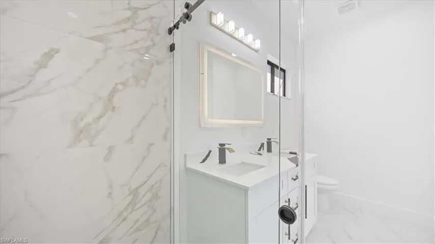 Bathroom featuring double vanity, light marble finish flooring, and a marble finish shower