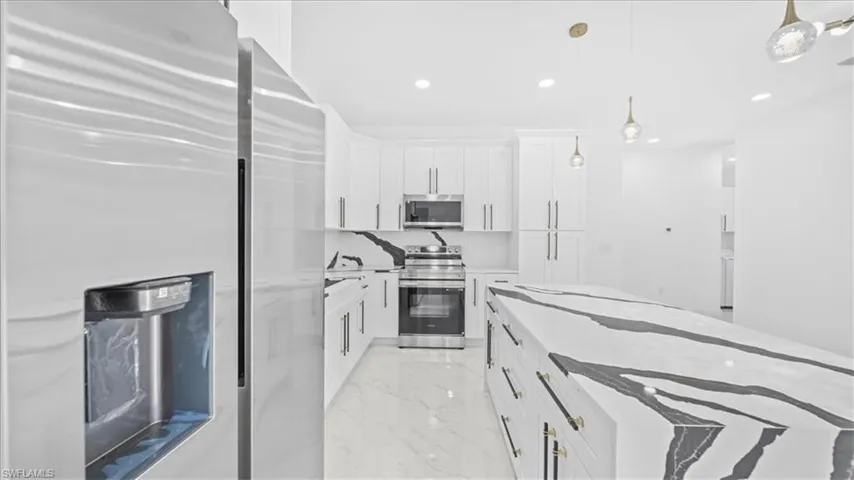 Kitchen with stainless steel appliances, hanging light fixtures, light stone countertops, and white cabinets
