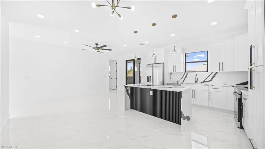 Kitchen with a kitchen island, white cabinetry, stainless steel appliances, and light stone counters