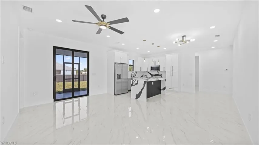 Kitchen with open floor plan, white cabinets, stainless steel appliances, and a kitchen island with sink