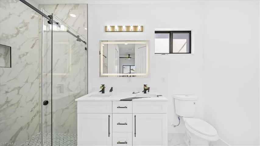 Full bath with a marble finish shower, double vanity, and light marble finish floors