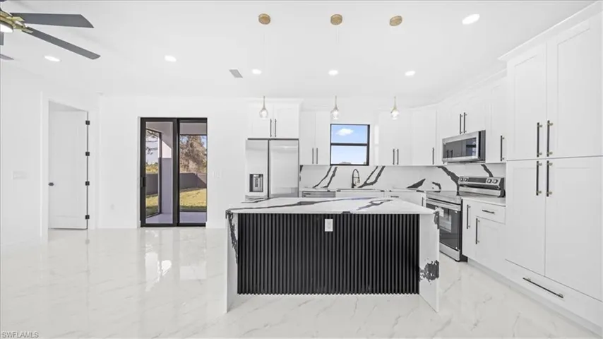 Kitchen featuring a center island, stainless steel appliances, white cabinets, pendant lighting, and light stone countertops