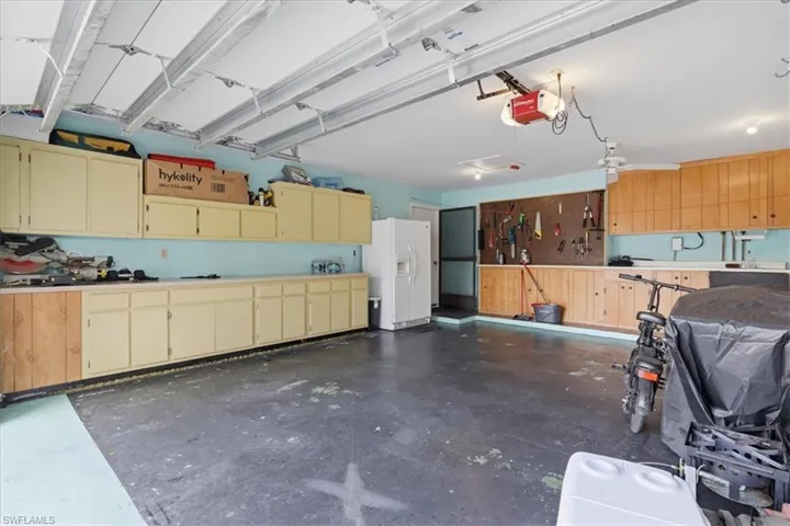 Garage with white refrigerator with ice dispenser and a garage door opener