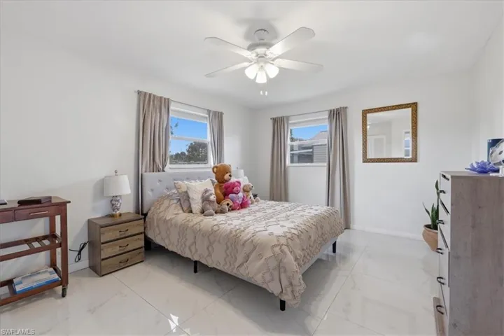 Bedroom with a ceiling fan, multiple windows, and light marble finish floors