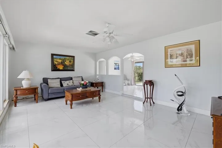 Living room featuring a ceiling fan, arched walkways, and light marble finish floors