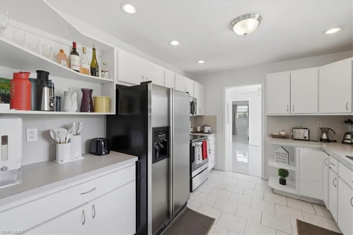 Kitchen with open shelves, white cabinets, light countertops, stainless steel appliances, and recessed lighting