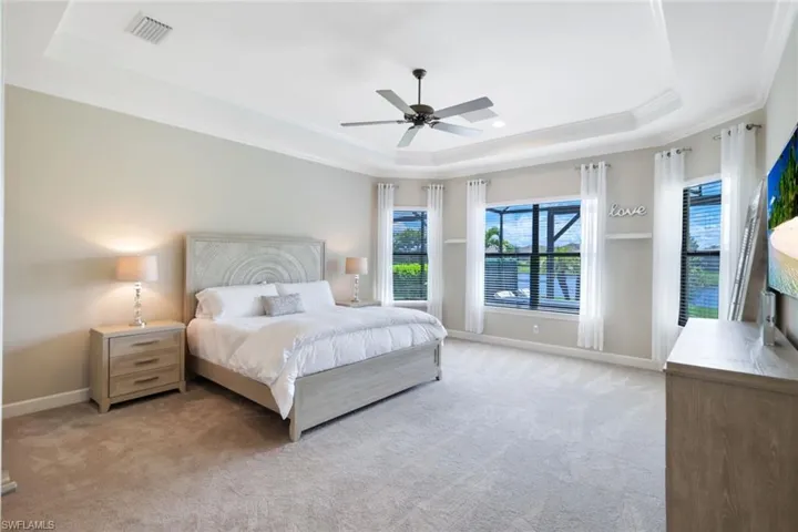 Bedroom featuring light carpet, ceiling fan, a raised ceiling, and crown molding