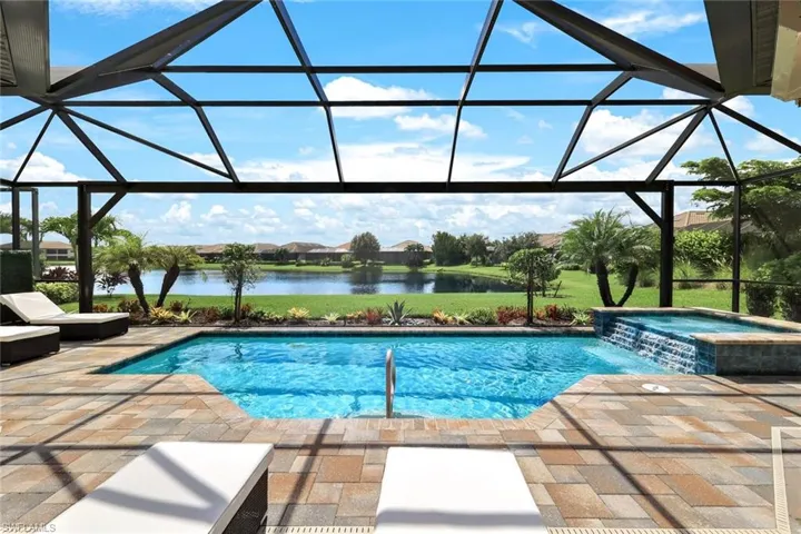 View of pool featuring a patio, a water view, a lanai, and an in ground hot tub
