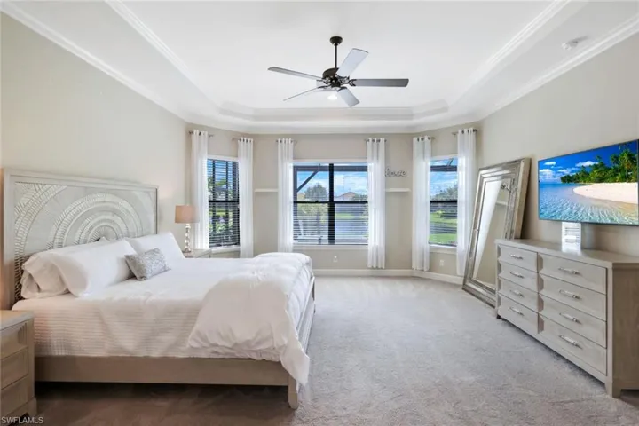 Primary Bedroom featuring ceiling fan, a tray ceiling, and light carpet