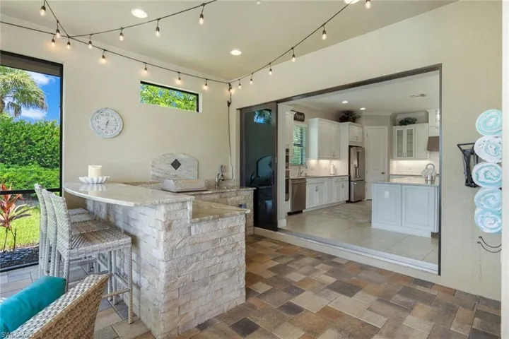Bar featuring light stone counters, white cabinets, stainless steel appliances, and a wealth of natural light