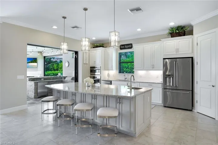 Kitchen with appliances with stainless steel finishes, white cabinets, quartz countertops, a center island with sink
