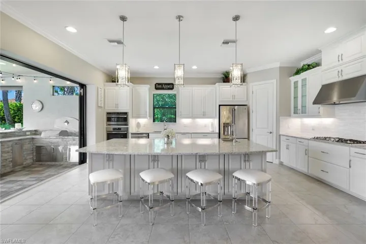 Kitchen with appliances with stainless steel finishes, a large island, quartz counters, and decorative light fixtures