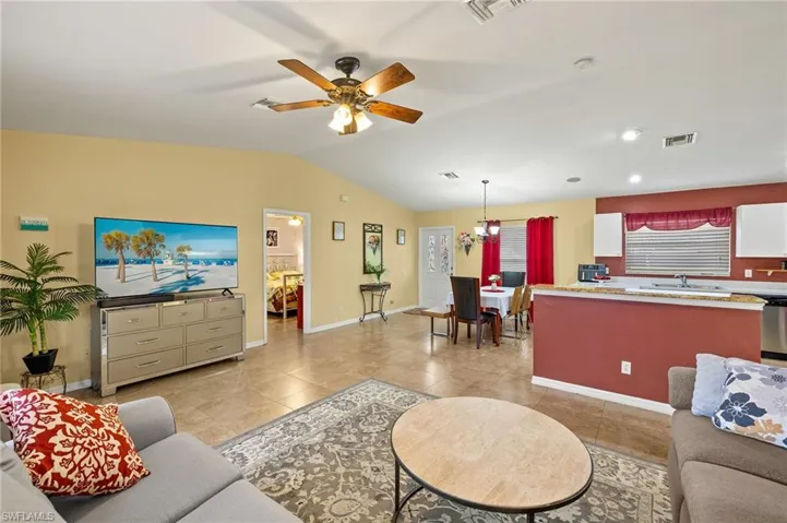Living area featuring visible vents, lofted ceiling, light tile patterned flooring, and ceiling fan with notable chandelier