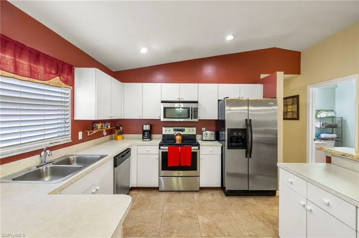 Kitchen featuring a sink, vaulted ceiling, light countertops, appliances with stainless steel finishes, and white cabinetry