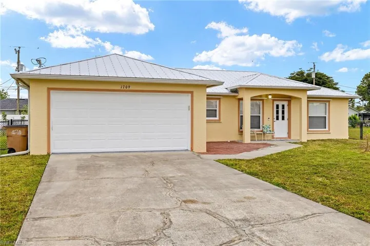 Single story home with concrete driveway, a front yard, stucco siding, metal roof, and a garage