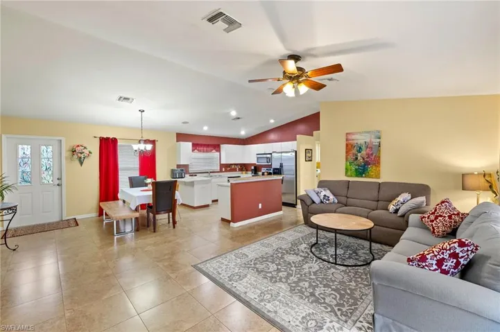Living area featuring light tile patterned flooring, visible vents, ceiling fan with notable chandelier, and vaulted ceiling