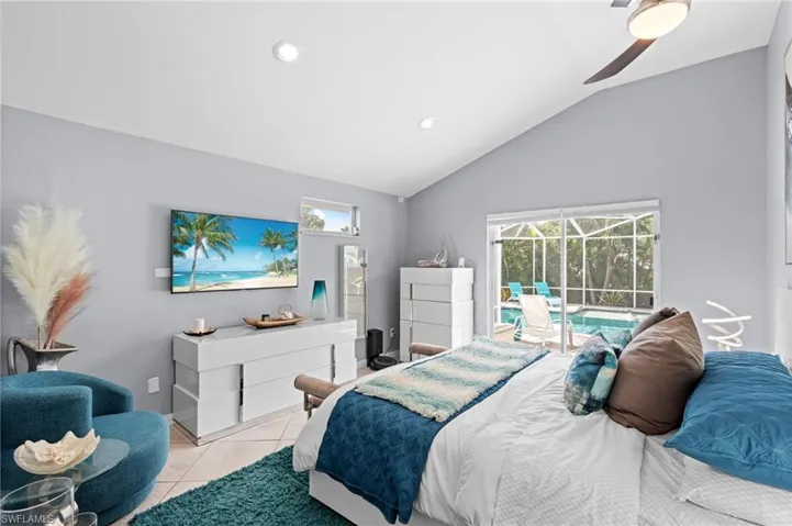 Tiled bedroom with ceiling fan, vaulted ceiling, access to exterior, and multiple windows
